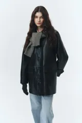 Chaqueta larga de cuero sintético color negro, de silueta amplia y estilo masculino. Presenta cierre frontal con botones, bolsillos delanteros con solapa y forro interior.