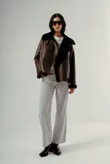 Chaqueta estilo aviador o biker de cuero marrón oscuro con forro y cuello de piel sintética negra. Presenta cierre asimétrico frontal y bolsillos laterales con cierre.