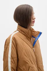 Campera acolchada color crema con cierre frontal y cuello alto. Presenta dos franjas azules en las mangas y ribete azul en el cuello y ruedo.