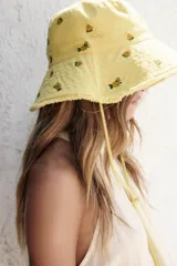 Gorro tipo bucket amarillo con bordado de flores y cordón ajustable.