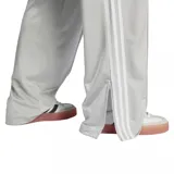 Pantalón Adidas Adicolor Classic Firebird color gris claro con tres tiras blancas a los costados, corte ancho, cintura elástica y logo bordado.