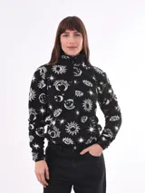 Buzo de polar tipo sherpa color negro con estampado de motivos celestiales como lunas, soles y estrellas. Presenta cuello alto con cierre frontal parcial y mangas largas.