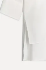 Camisa extra larga blanca de popelín de algodón, con cuello solapa, manga larga con puños, pinzas en la espalda, aberturas laterales y cierre frontal con botones.
