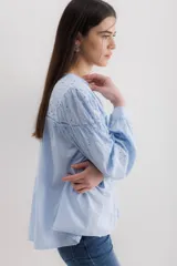 Camisa celeste de algodón con bordado calado, cuello en V y mangas largas abullonadas con puños elásticos.
