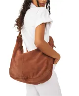 Bolso tipo hobo de gamuza negra, con forma holgada y cierre principal de cremallera. Se lleva al hombro con dos asas de correa delgadas sujetas con argollas metálicas plateadas.