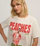 Remera color crudo de algodón con estampado frontal de Justin Bieber y la palabra "Peaches" en rojo.
