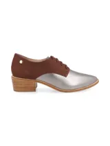 Zapato acordonado de cuero color plateado con puntera fina y detalle de cuero marrón en el talón.