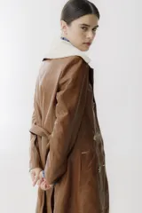 Trench de cuero color camel con cuello de piel sintética color crema, doble botonadura, bolsillos laterales y corte evasé.