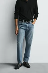 Jeans de denim de algodón, color negro lavado, con tiro medio, corte ajustado en cadera y muslos, y pierna que se estrecha hacia el tobillo. Presenta cinco bolsillos y cierre frontal con cremallera y botón.