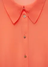 Blusa color salmón de tejido fluido semitransparente, con cuello camisero, manga larga con puños abotonados y cierre frontal con botones.