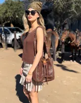 Bolso tipo bucket de cuero color marrón con tachas plateadas. Tiene correa larga regulable para usar al hombro y cierre con cordón ajustable.