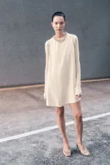 Vestido corto sin mangas color beige. Modelo levemente evasé con escote redondo, abertura de cerradura con botón oculto en la nuca y bajo recto. Parcialmente forrado.