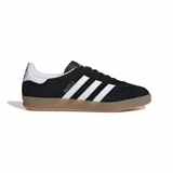 Zapatillas Adidas Gazelle Indoor negras con las tres tiras laterales blancas, detalle dorado con el nombre del modelo y suela de goma color caramelo.