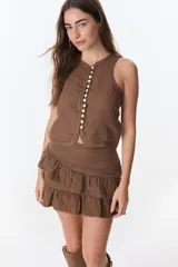 Top sin mangas color beige, con escote en V y cierre frontal de botones de nácar. Presenta costuras decorativas en el borde del escote y sisas.