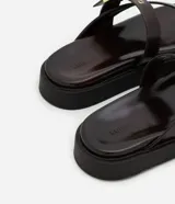 Sandalias planas de PU color marrón oscuro, con tira entre los dedos y tira ancha sobre el empeine con hebilla dorada ajustable.