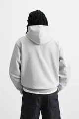 Sudadera con capucha gris confeccionada en tejido de algodón con interior rizo. Tiene manga larga, bolsillo frontal tipo canguro y acabados en rib.