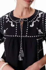 Blusa negra con bordados blancos de animales y motivos geométricos. Tiene cuello redondo con lazo y mangas cortas.