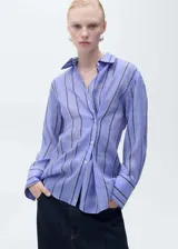 Camisa celeste con rayas verticales blancas y grises, de corte oversize, cuello camisero y mangas largas con puños abotonados.