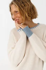 Sweater de punto color crudo con cuello redondo y terminaciones en celeste.
