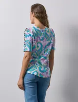 Remera estampada con diseño paisley en tonos celeste, rosa, amarillo y verde. Tiene mangas cortas con detalle de aberturas y lazos en los hombros.