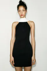 Minivestido negro con cuello halter y espalda descubierta. Presenta un panel blanco en la parte superior delantera y forro interior.