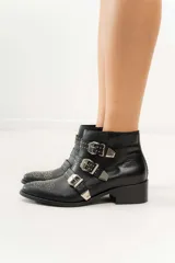 Botas cortas de cuero negro con puntera fina, taco bajo y cierre lateral. Presentan tres correas con hebillas plateadas y apliques de tachas plateadas.
