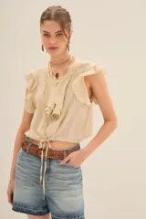 Camisa color crema de corte corto con escote redondo, mangas cortas con volados y jareta ajustable en el ruedo.