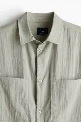 Camisa color verde claro con cuello inglés, tapeta lisa y canesú en la espalda. Modelo de manga corta con dos bolsillos superiores abiertos y bajo recto con aberturas laterales.