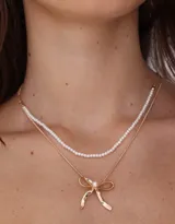 Collar corto doble, con cadena superior de perlas y cadena inferior dorada con dije de moño.