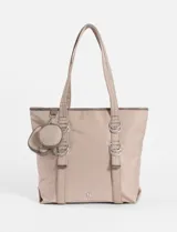 Cartera tipo shopper color beige, con asas de hombro y detalles de argollas metálicas. Incluye dos monederos redondos removibles colgando de una de las asas.