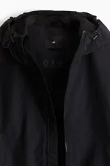 Campera rompevientos negra de nylon repelente al agua con protección UV, corte regular, cierre frontal, capucha con cordón de ajuste elástico, puños elásticos, bolsillos laterales y bolsillo interior con cierre, forro de malla y cordón de ajuste elástico oculto en el bajo.