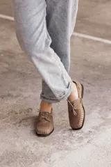 Mocasín de cuero negro con cordones y tachas metálicas en la puntera.