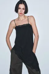 Top negro con estampado de lunares blancos, escote recto, tirantes finos, detalle de encaje en el escote y bajo asimétrico con abertura lateral.