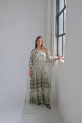 Vestido largo color blanco con estampado geométrico en verde y ocre. Tiene cuello mao, mangas largas abullonadas y corte imperio con falda escalonada.