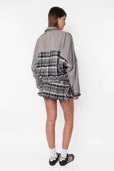 Minifalda gris con estampado de cuadros escoceses, cintura ancha, tablas en la parte inferior y cierre metálico lateral. Incluye sobrefalda desmontable con bolsillo.