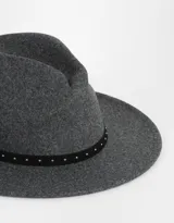 Sombrero fedora gris con cinta negra decorada con tachas plateadas.