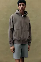 Campera con capucha color marrón topo, corte oversized, con cierre frontal, bolsillos tipo canguro, puños y bajo acanalados.