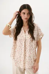 Blusa color crema con estampado de hojas marrones, escote en V y mangas cortas con dobladillo.