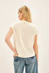 Remera color crema de calce suelto, confeccionada en viscosa. Tiene escote redondo, manga corta y estampa frontal centrada con bordado.