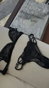 Conjunto de lencería de encaje negro, compuesto por un corpiño triangular con breteles regulables y una bombacha less con tiras regulables.