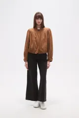 Campera marrón de manga larga con cuello mao y cierre frontal de un solo botón. Presenta pinzas y frunces en el canesú delantero y en los hombros, creando un efecto abullonado en las mangas. El bajo es ajustado con elástico.