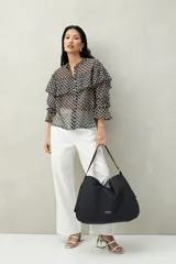 Camisa negra semitransparente de encaje bordado con diseño geométrico. Tiene silueta fluida, mangas largas y volados en el frente y los hombros.