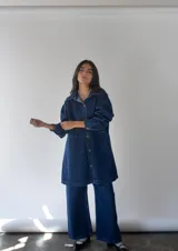 Vestido camisero largo de denim azul con botones frontales, cuello camisero, mangas largas y bolsillos de parche en el pecho.