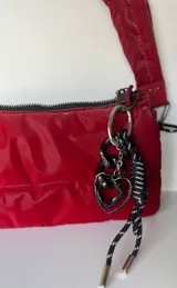 Llavero con cadena de eslabones plateados y charms colgantes: cadena de eslabones gruesos negros, cordón trenzado negro y blanco, y dije de corazón plateado.
