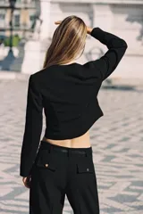 Pantalón tobillero negro de tiro alto con cinturón de cadena dorada. Presenta falsos bolsillos con solapa en la espalda, pernera recta y cierre lateral con cremallera oculta.