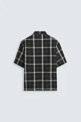 Camisa de hombre relaxed fit con estampado de cuadros blancos sobre fondo negro, cuello solapa, manga corta y cierre frontal con botones.