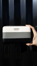 Billetera mediana de símil cuero con diseño a rayas horizontales en blanco, gris y negro. Tiene cierre alrededor y tapa frontal con compartimento interior con 8 tarjeteros y lugar para billetes.
