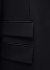 Blazer negro de corte recto con cuello de pico con solapa, tres bolsillos de solapa en la parte frontal y manga larga con puños abotonados.