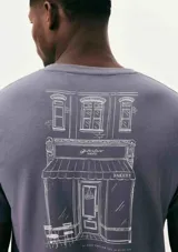 Camiseta blanca de algodón con cuello redondo y mangas cortas. Estampa rectangular con borde negro que contiene la frase "NATURAL ATMOSPHERE" en letras mayúsculas y una imagen de montañas y mar.