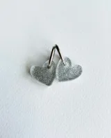 Par de aros colgantes con forma de corazón plateado con glitter y argolla metálica plateada.